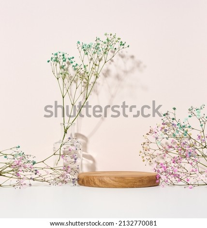 stage for displaying products, cosmetics with a round wooden podium and a glass vase with a bouquet of flowers. beige background Royalty-Free Stock Photo #2132770081