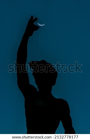 The beautiful vertical shot of the boy silhouette holding a half-moon view in his right hand isolated on a blue background