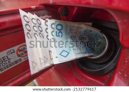 Banknotes (Polish zlotys) in the fuel filler of a red car. A fuel tank consumes money. Fuel prices increase causing money to be sucked into fuel tanks.  Royalty-Free Stock Photo #2132779617
