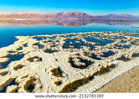 Evaporated salt forms bizarre patterns on the water. Dead Sea. The blue water is surrounded by pink mountains. Sunny winter day. The picture was taken by a drone from a aerial view. Israel. 
