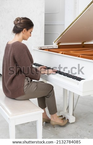 A young woman in elegant casual clothes plays the grand piano on a white background
