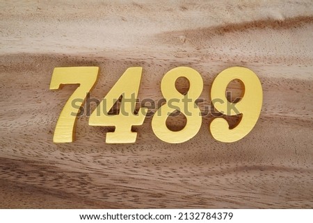 Wooden  numerals 7489 painted in gold on a dark brown and white patterned plank background.