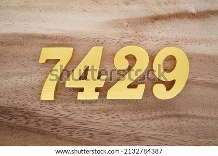 Wooden  numerals 7429 painted in gold on a dark brown and white patterned plank background.