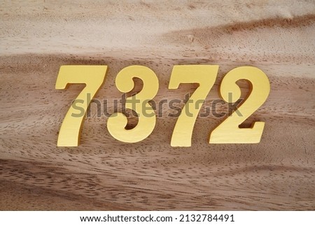 Wooden  numerals 7372 painted in gold on a dark brown and white patterned plank background.