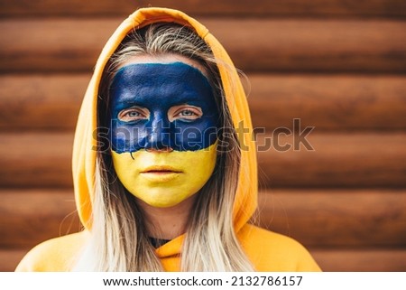 Outdoor portrait of young girl with blue and yellow ukrainian flag on her face. Stop war in Ukraine. Russia stop war.