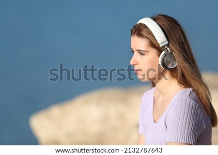 Profile of a relaxed teen wearing wireless headphones contemplating views listening to music in a lake or beach