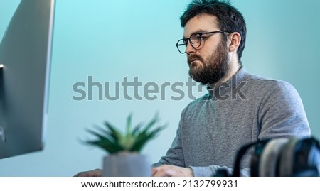 A man with glasses and a beard in front of a computer screen.