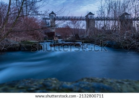 A long exposure at sunrise at a weir on the Ruhr River. In the foreground are stones in the water.