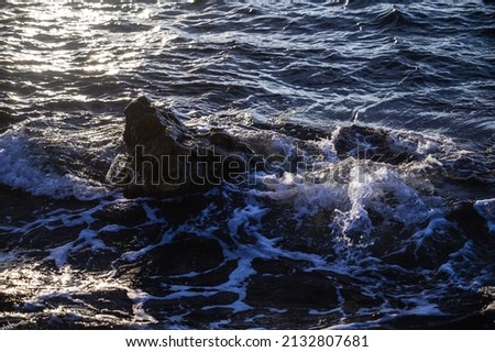 The blue sea storms at sunset, the waves wash the stone sticking out of the water