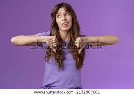 Unimpressed ignorant snobbish attractive curly-haired girl disagree lame idea look away disappointed show thumbs down dislike disapproval gesture not interested upset purple background Royalty-Free Stock Photo #2132809601