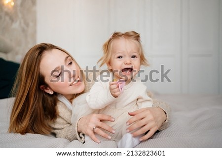 Cute mom and baby daughter lie down, play and hug in bed. games with children. cozy and beautiful home clothes. psychological support for single mothers. happy childhood about motherhood. Royalty-Free Stock Photo #2132823601