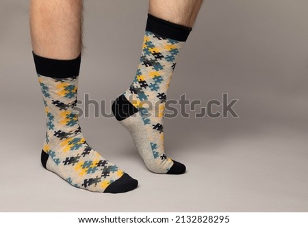 Studio photo of a pair of feet wearing  colourful patterned socks. The man wearing the socks is caucasian. The background is grey.