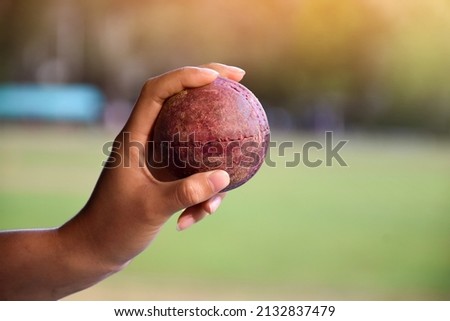 Old leather cricket ball holding in hand of student in front of school cricket court, soft and selective focus on ball, traditional sport and cricket sport lover around the world concept.