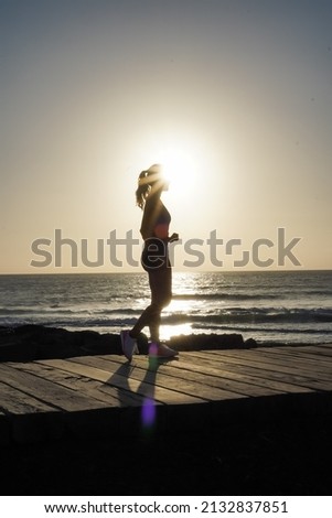 silhouette of a running sportive athletic woman on beach boardwalk during sunset 
