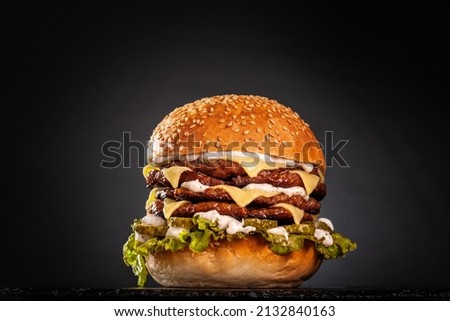Quadruple burger with cheese cucumber and lettuce. Isolated on black background. Royalty-Free Stock Photo #2132840163