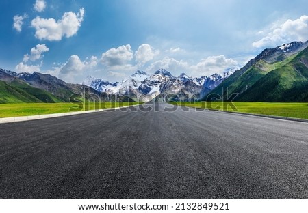 Straight asphalt road and green grass with snow mountain nature scenery under blue sky. Road and mountains background. Royalty-Free Stock Photo #2132849521