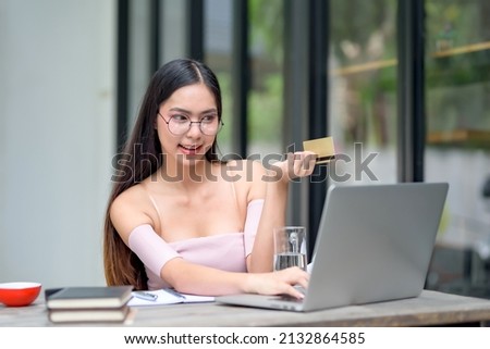Beautiful Asian woman holding credit card and using laptop enjoying online shopping.