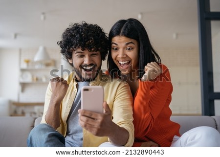 Excited friends using smartphone  playing mobile game relaxing at home. Happy emotional couple win online lottery celebration success. Multiracial students reading test results   Royalty-Free Stock Photo #2132890443