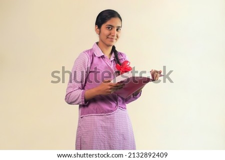 A school girl looking at camera with smile while holding book in her hand Royalty-Free Stock Photo #2132892409