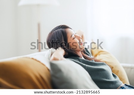 Closeup - Relaxed young asian woman enjoying rest on comfortable sofa at home, calm attractive girl relaxing and breathing fresh air in home, copy space. Royalty-Free Stock Photo #2132895665