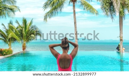 An unidentified caucasian woman tightened her hair before stepping into a pool. There are the sea, mountains and coconut trees in front of her Royalty-Free Stock Photo #2132899977