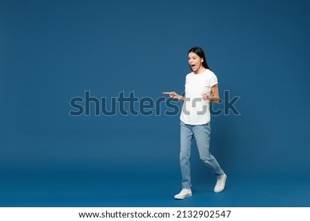 Full length young shocked surprised latin woman 20s wearing white casual basic t-shirt do winner gesture clench fist celebrating look aside isolated on dark blue color background studio portrait