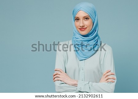 Young smiling confident arabian asian muslim woman in abaya hijab hold hands crossed folded isolated on plain blue color background studio portrait. People uae middle eastern islam religious concept Royalty-Free Stock Photo #2132902611