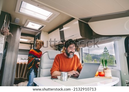 Daily normal life inside a camper van rv mobile home. Woman cooking in the kitchen and adult man working on laptop computer. Outdoors park nature outside the window. Freedom vanlife people lifestyle Royalty-Free Stock Photo #2132910713