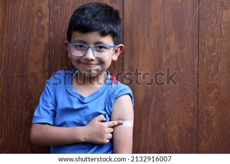 Little 6-year-old Latino boy with glasses and a blue shirt shows his arm with a bandage because he has just been vaccinated against Covid-19 in the new normality due to the Coronavirus pandemic
 Royalty-Free Stock Photo #2132916007
