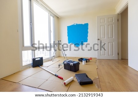Empty room interior with a wooden floor and a half painted blue wall - A ladder and tins of paint Royalty-Free Stock Photo #2132919343