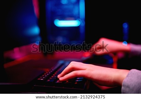 Teenager boy play computer video game in dark room, use neon colored rgb mechanical keyboard, workplace for cybersport gaming