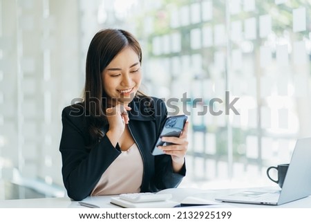 Asian businesswoman in formal suit in office happy and cheerful during using smartphone and working Royalty-Free Stock Photo #2132925199