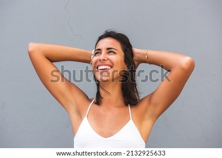 Close up portrait young woman laughing with hands in hair by gray background 