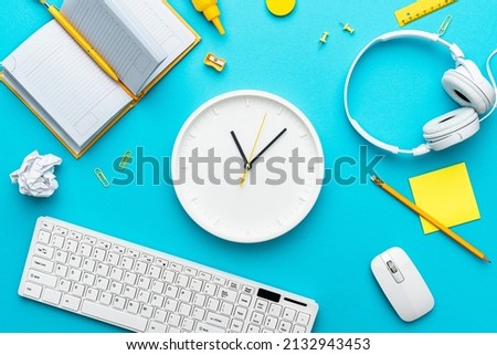 View from above on the office table with watch as working day concept. Flat lay image of office and deadline concepts over turquoise blue background. Top-down composition of time management concept.