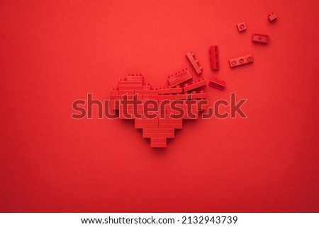 Red falling apart heart symbol made of plastic building blocks. Flat lay image of breaking down like button on red background. Minimalist photo of stylized dissolving love symbol. Royalty-Free Stock Photo #2132943739