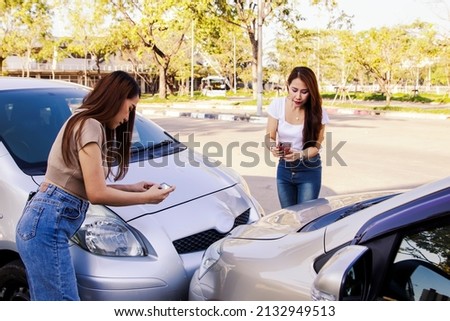 Two young women driving a car collide on a lane breaking traffic rules are using smartphones to take pictures together as evidence for car insurance claims : Accident and car insurance concept. Royalty-Free Stock Photo #2132949513