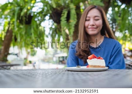 Blurred image of a young woman looking at a piece of strawberry cheese cake on the table