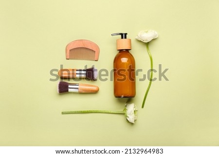 Bottle of cosmetic product, makeup brushes, hair comb and ranunculus flowers on green background