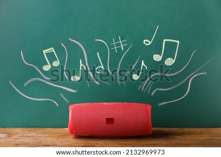 Modern wireless portable speaker and drawing of music notes on color background