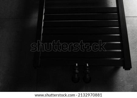 Picture of black matte heated towel rack, in the bathroom with dark grey walls.