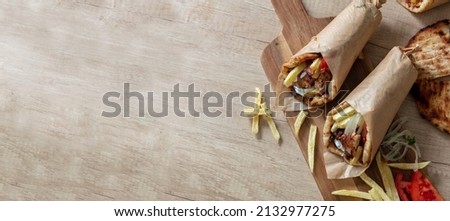 Gyro pita Shawarma preparation on wooden table, top view. Greek food, sliced meat, potato, tomato and tzatziki, paper wrap. Banner, Copy space
 Royalty-Free Stock Photo #2132977275