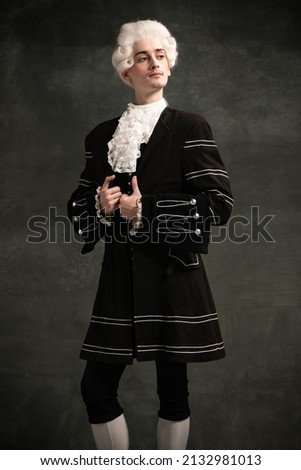 Young man in image of Amadeus Mozart, medieval person isolated on dark vintage background. Retro style, comparison of eras concept. Elegant male model as historical character, great music compose Royalty-Free Stock Photo #2132981013
