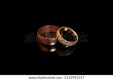 Two gold wedding rings on a black background with reflection