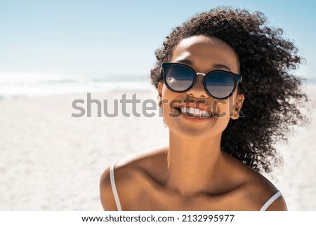 Portrait of smiling black woman wearing fashion sunglasses at the beach with copy space. Pretty african american girl wearing specs at the seaside during summer vacation. Beautiful young woman at sea  Royalty-Free Stock Photo #2132995977