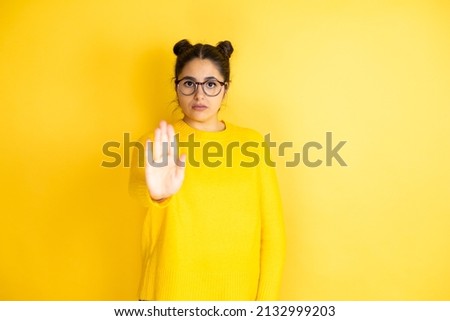Young beautiful woman wearing casual sweater over isolated yellow background serious and doing stop sing with palm of the hand.