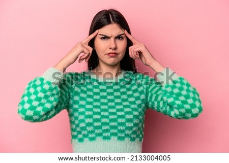 Young caucasian woman isolated on pink background focused on a task, keeping forefingers pointing head.