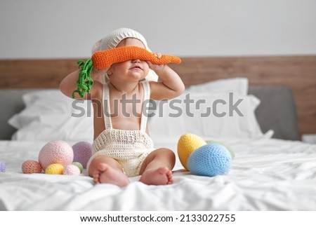Little baby in rabbit costume covering eyes with big carrot  