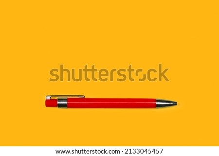 A red ballpoint pen on a yellow background with copy space