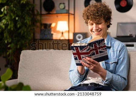 A cheerful handsome teenage boy learns English using a dictionary. A student is preparing for a college exam. Royalty-Free Stock Photo #2133048759