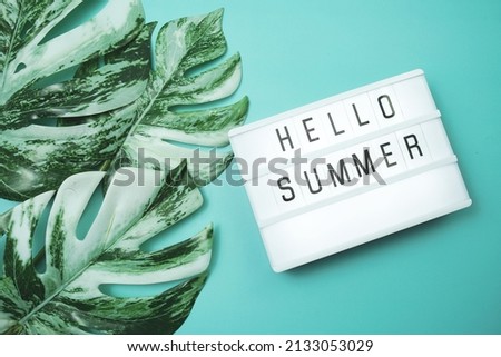 Hello Summer word in lightbox with Monstera Leaves on blue background